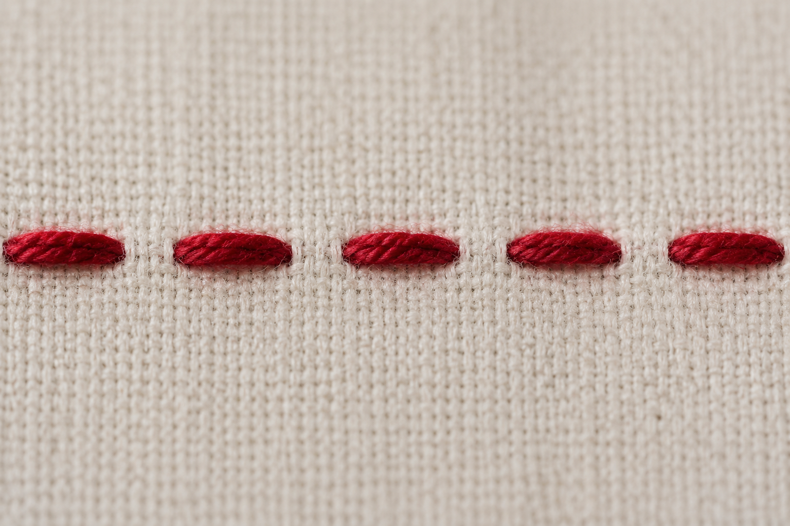Single row of red running stitches across cream linen